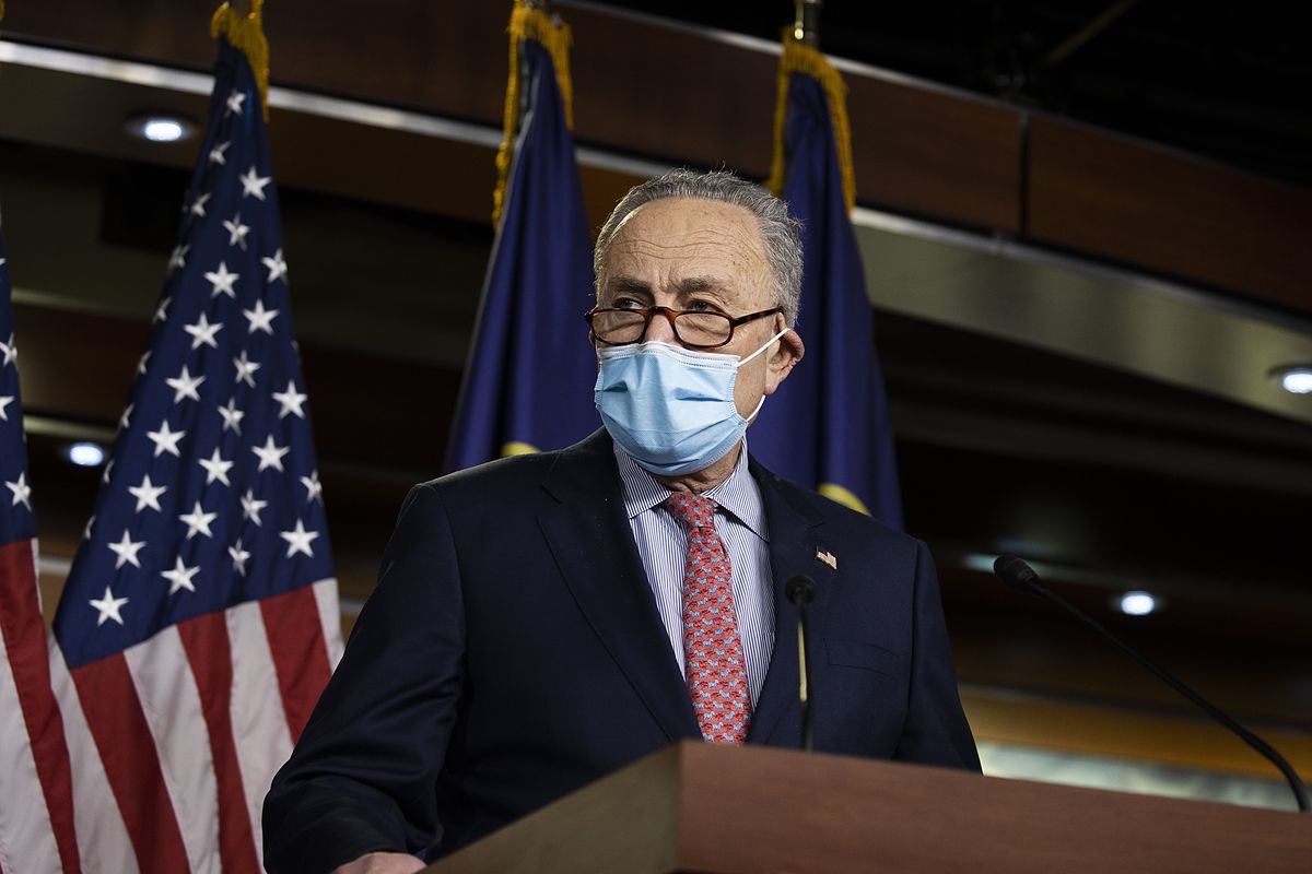 Chuck Schumer wearing a mask stands at a podium. 