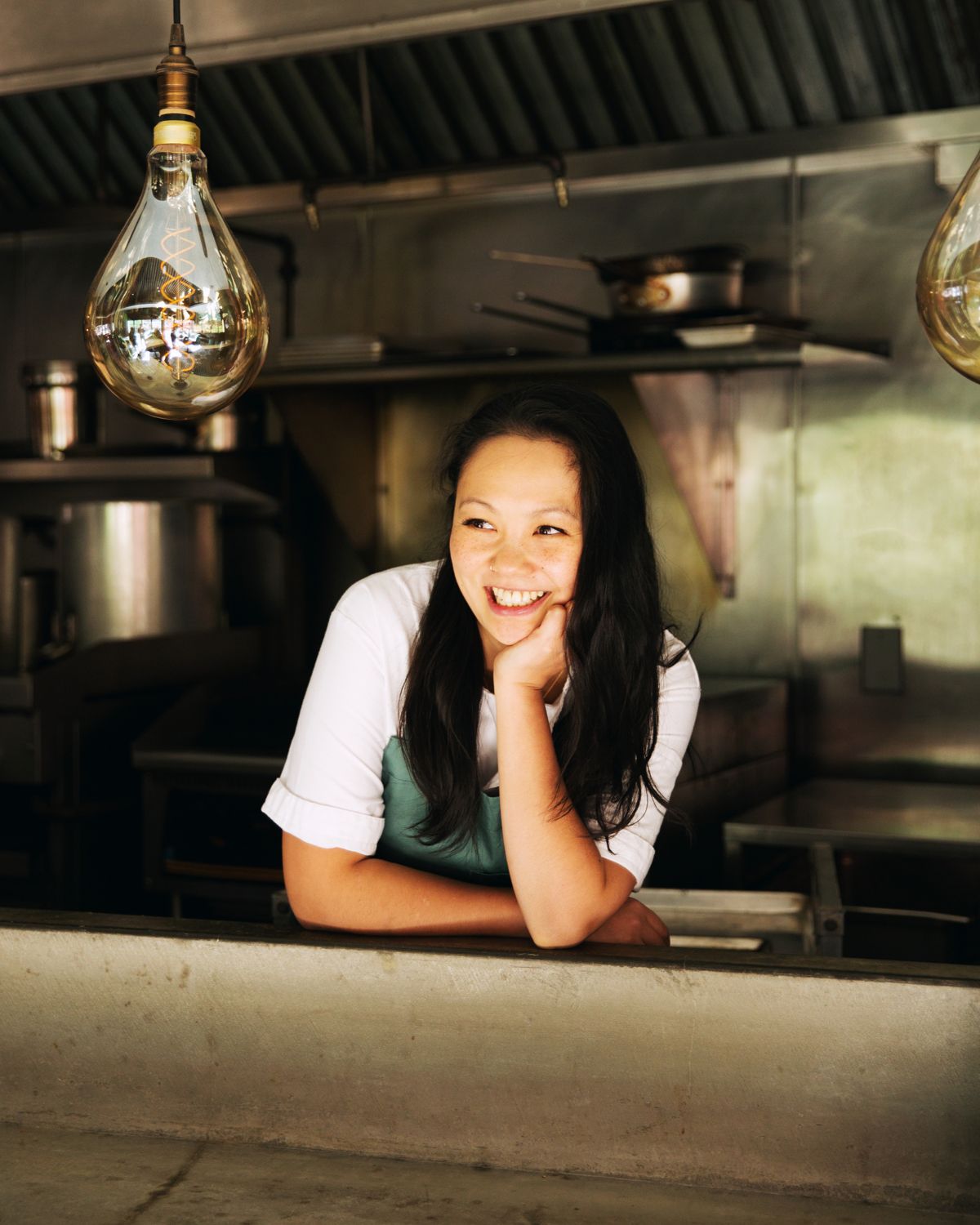 A chef leans on a counter, the oven behind her.