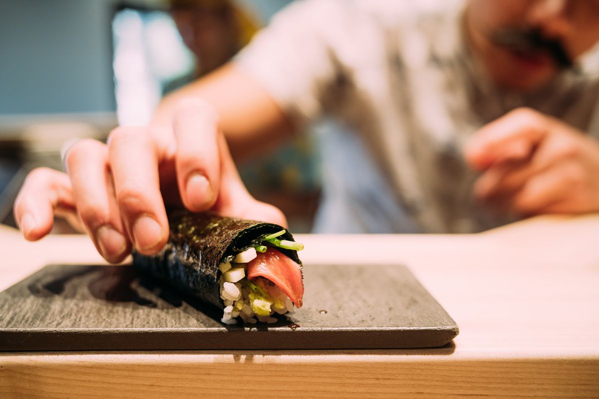 A chef places a crab-stuffed handroll on a serving plate.