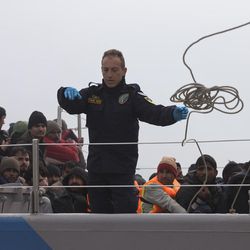 A Greek coast guard vessel crew member throws a rope to anchor the ship after a rescue operation of 127 refugees and migrants off the shores of the Greek island of Lesbos, Tuesday, March 22, 2016.  Greece detained hundreds of refugees and migrants on its islands Monday, as officials in Athens and the European Union conceded a much-heralded agreement to send thousands of asylum-seekers back to Turkey is facing delays. 