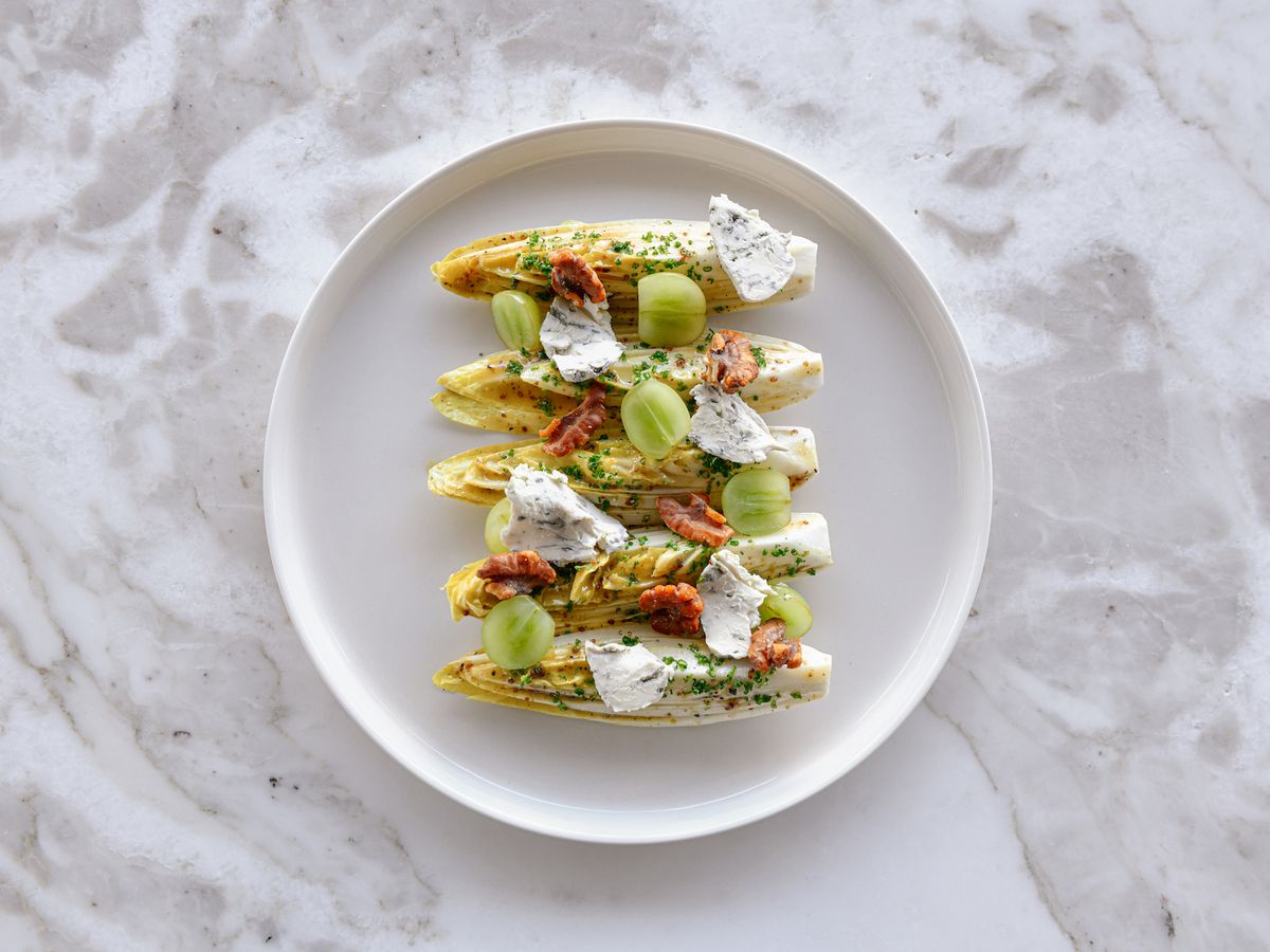 An overhead shot of four lines of endive with creme fraiche on a marble table.