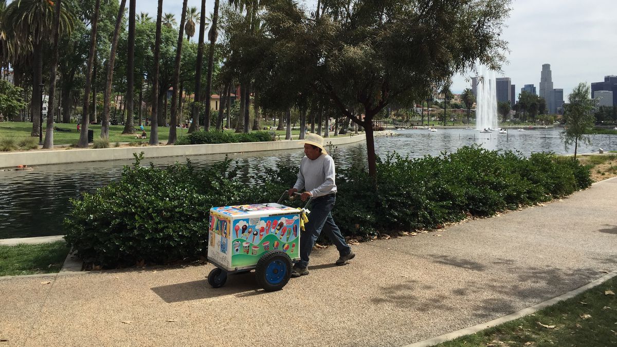 A vendor sells at Echo Park Lake on a sunny day, pushing a cart of paletas.