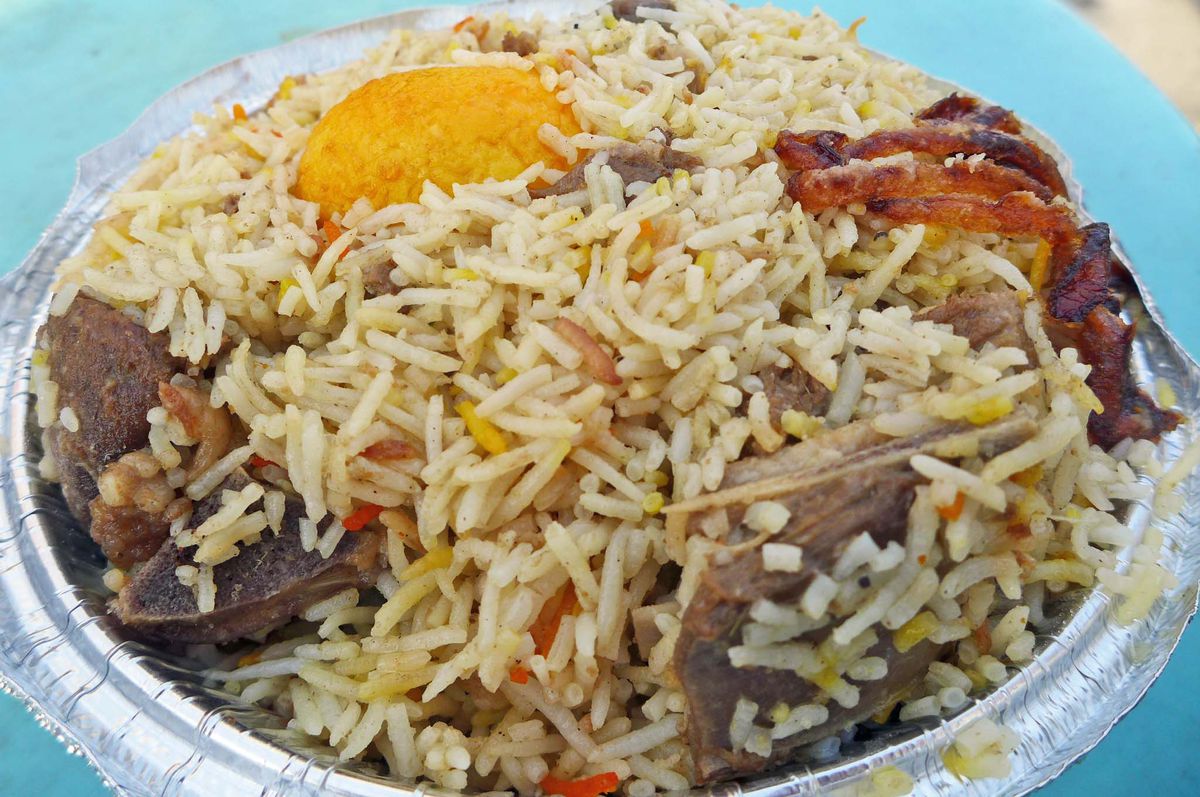 A metal carryout container with biryani and a battered and fried boiled egg.