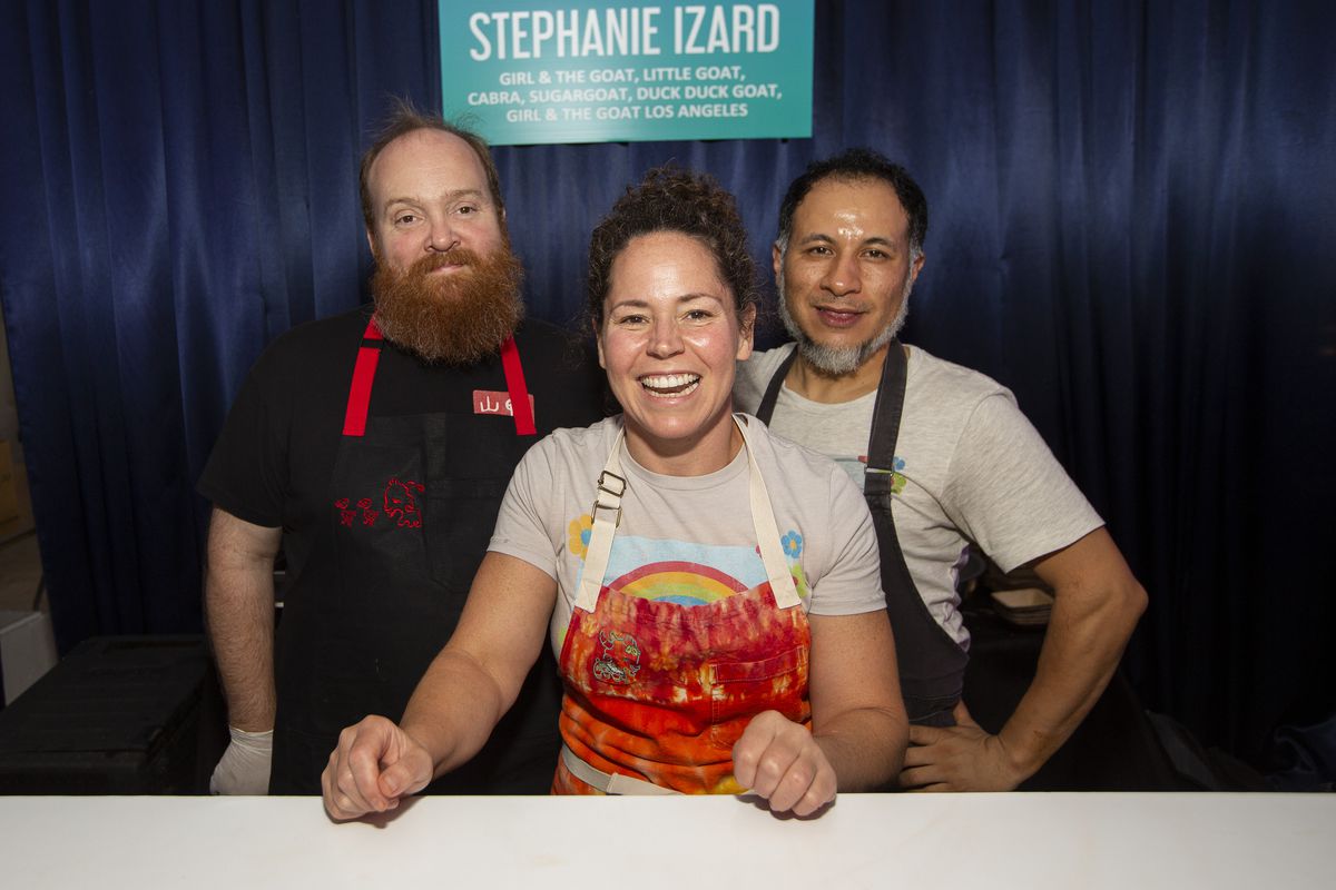 Stephanie Izard and two male chefs wearing aprons smile and pose for the camera.