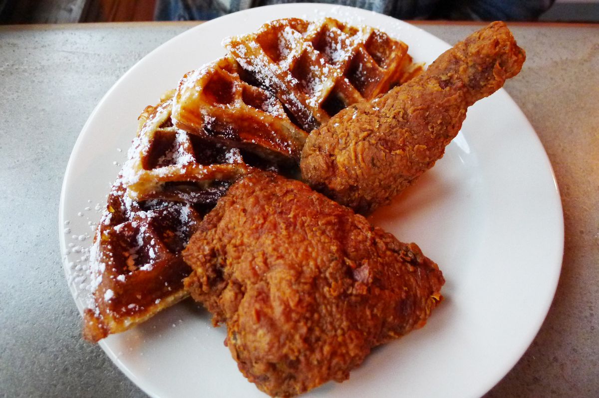 Two pieces of fried chicken and two half waffles sprinkled with powdered sugar