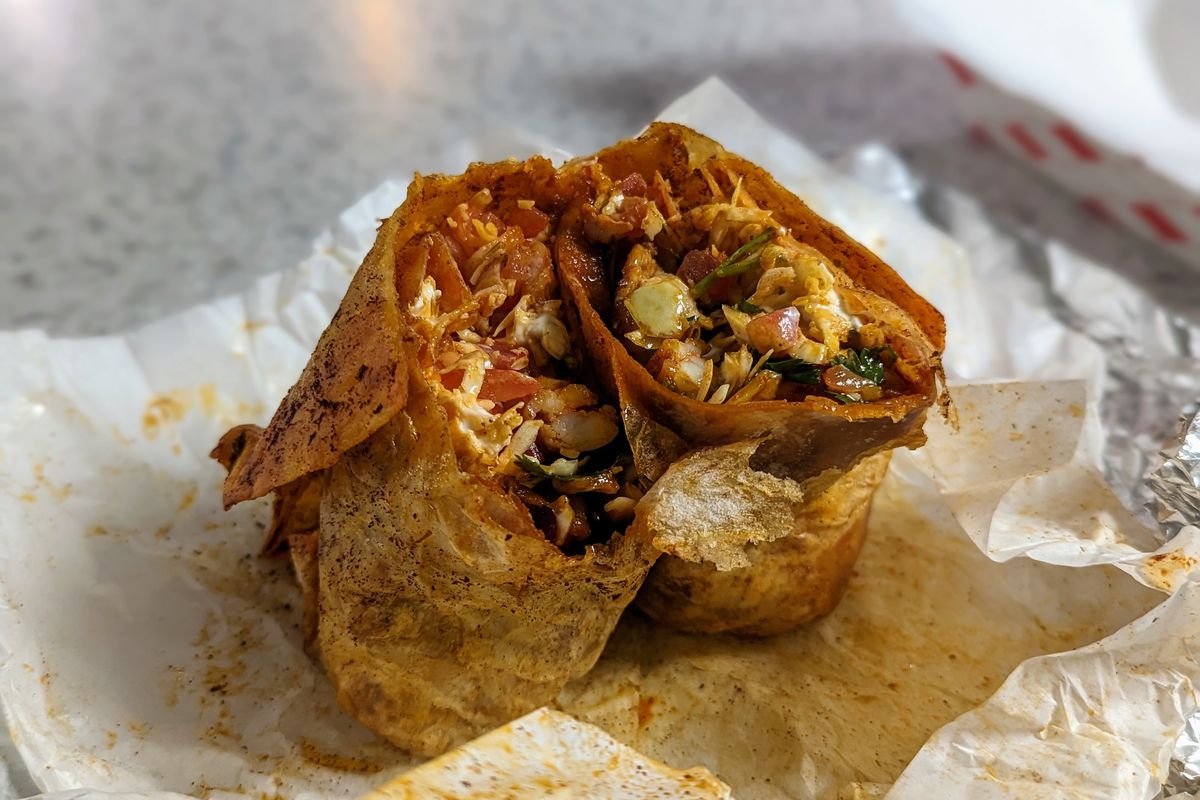Paper around a seasoned burrito filled with grilled shrimp.