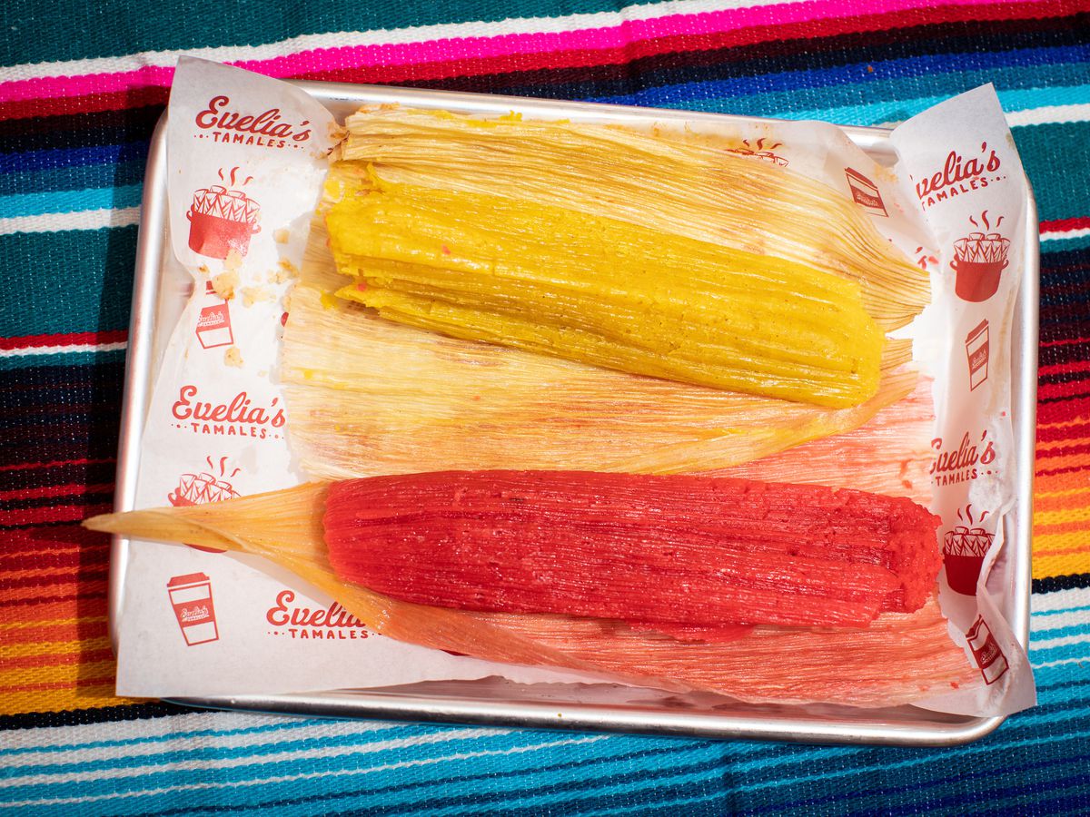 Yellow and red tamales, made with pineapple and raisins respectively, bask on a stainless steel tray.