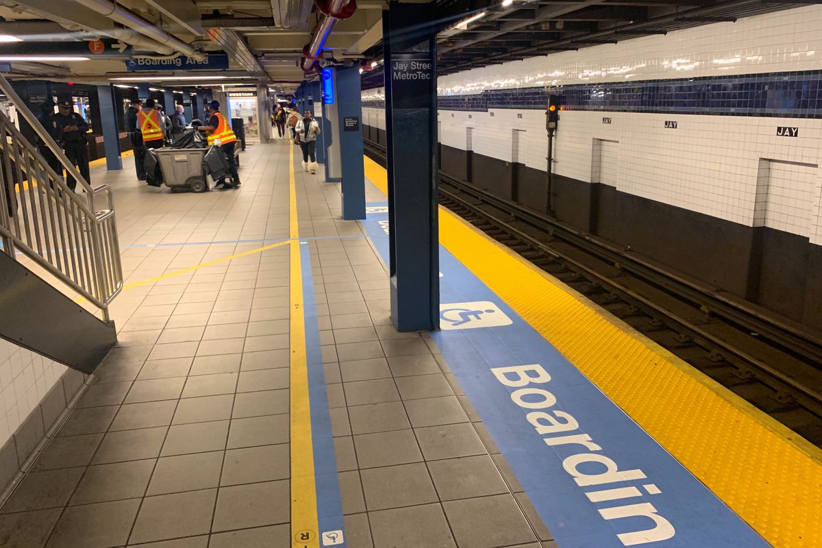 Blue signage on the floor of the Jay Street-Metro Tech station states, “Boarding” beside yellow tactile guides designed to help visually impaired passengers onto trains at the edge of the subway platform.