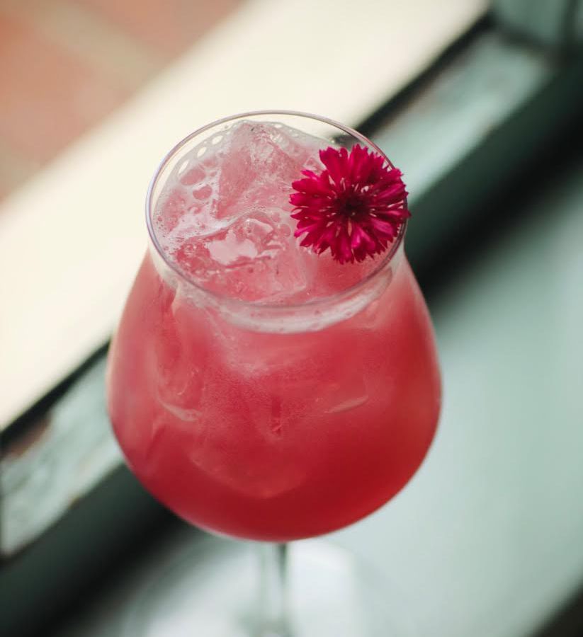A pink-hued drink in a glass with a pink flower garnish