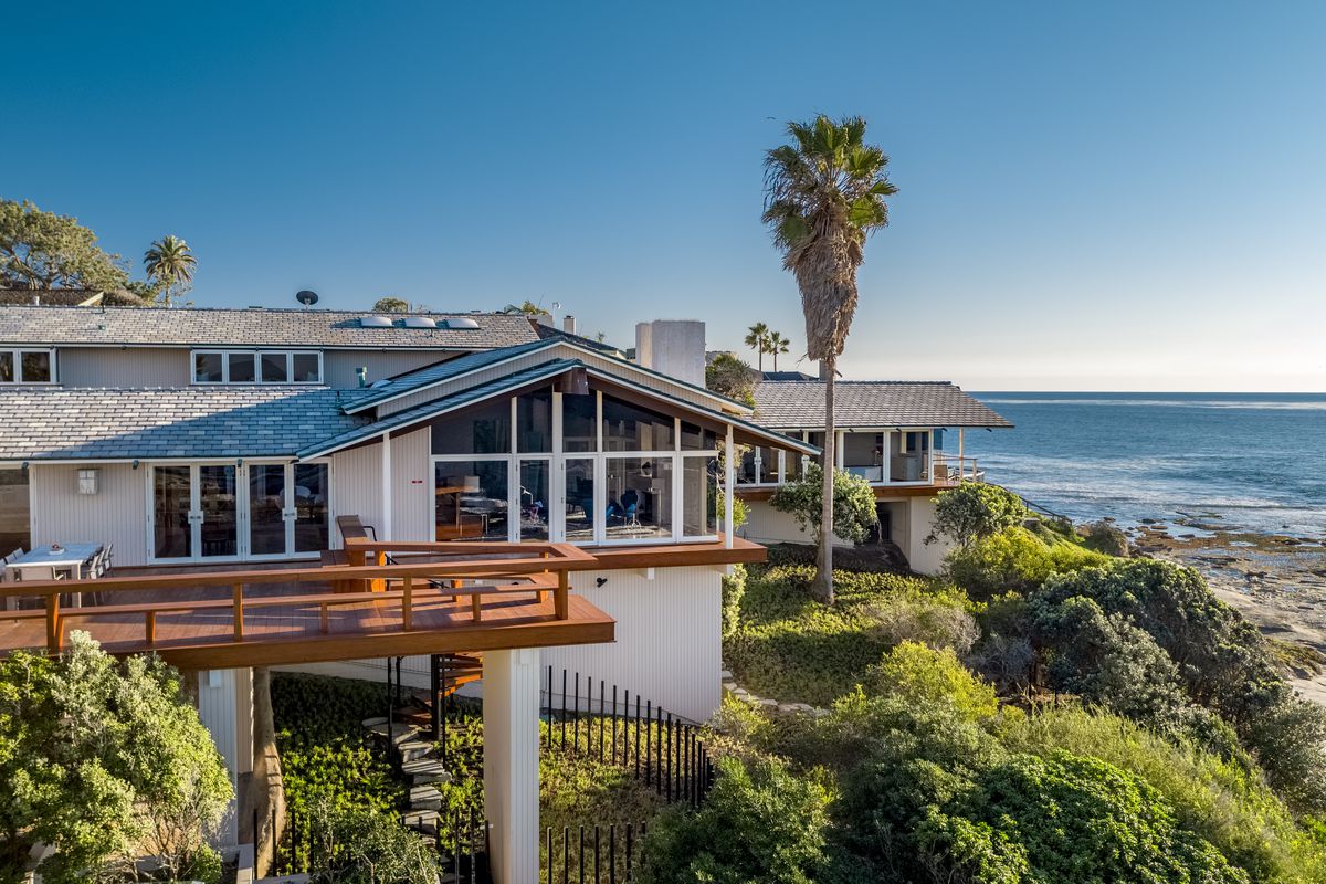 An exterior view of an oceanfront home with lots of windows and decks. A palm tree rises next to the house and you can see the ocean in the distance.
