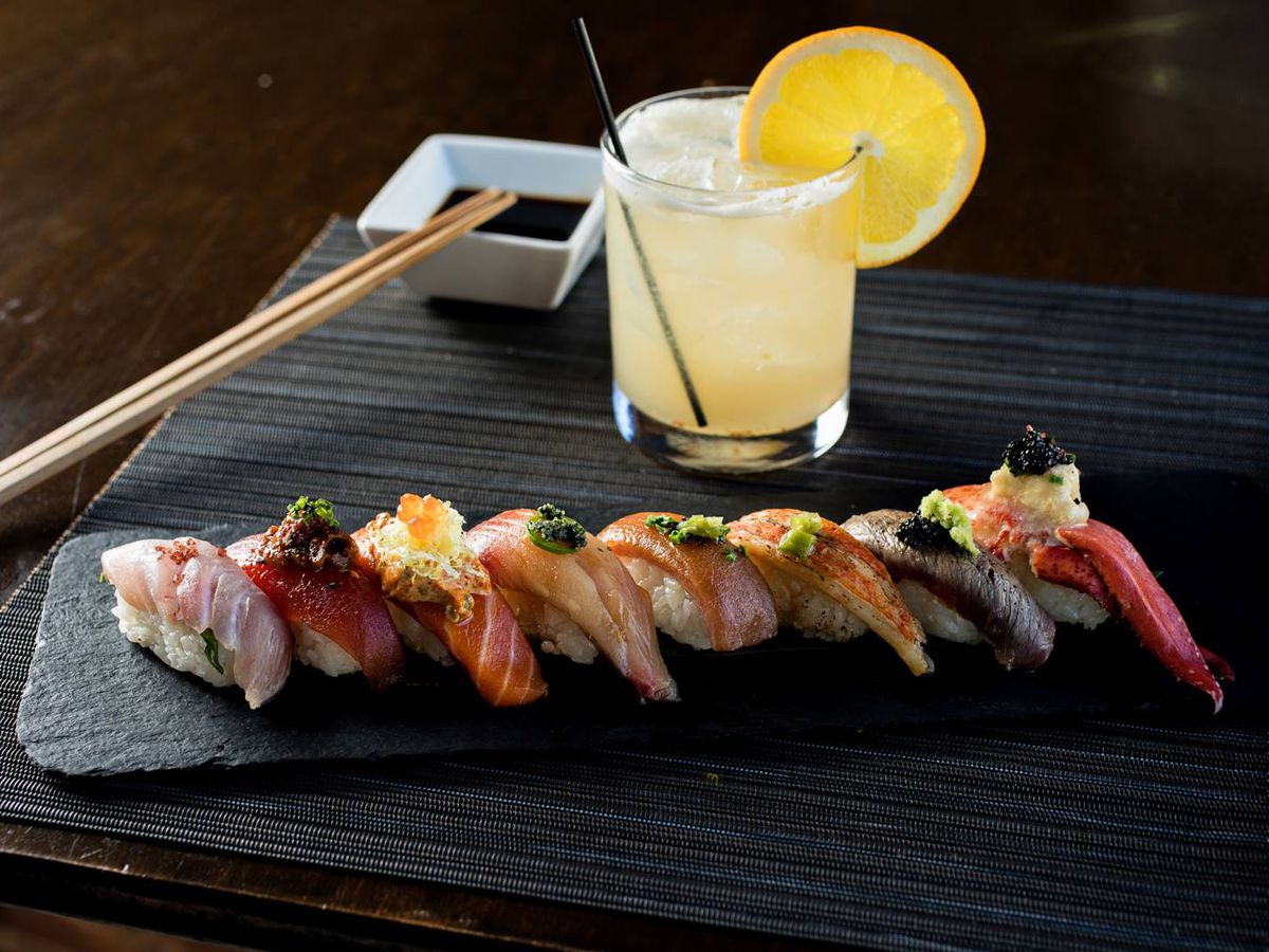 A line of nigiri next to a yellow cocktail. 