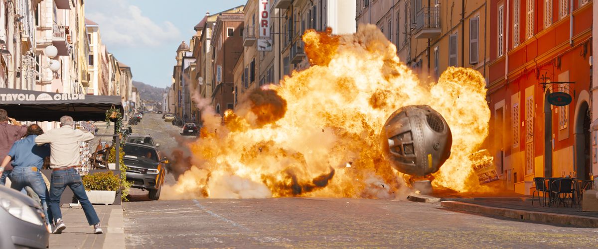 A giant flaming spherical metal bomb rolls through the streets of Rome, smashing vehicles, in an action scene in Fast X