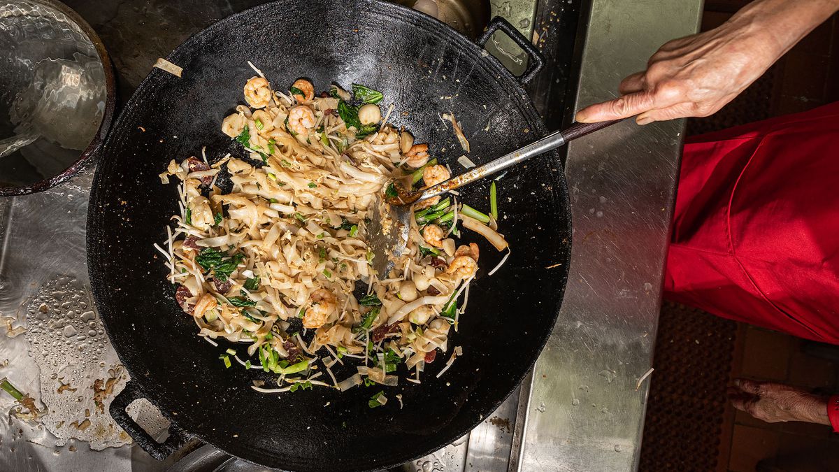 Rice noodles with shrimp and vegetables being prepared in a wok.