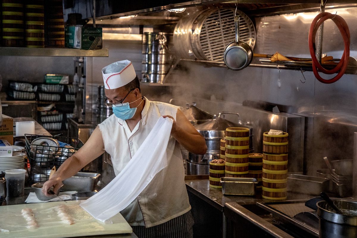 A chef in a face covering is preparing dim sum in a kitchen