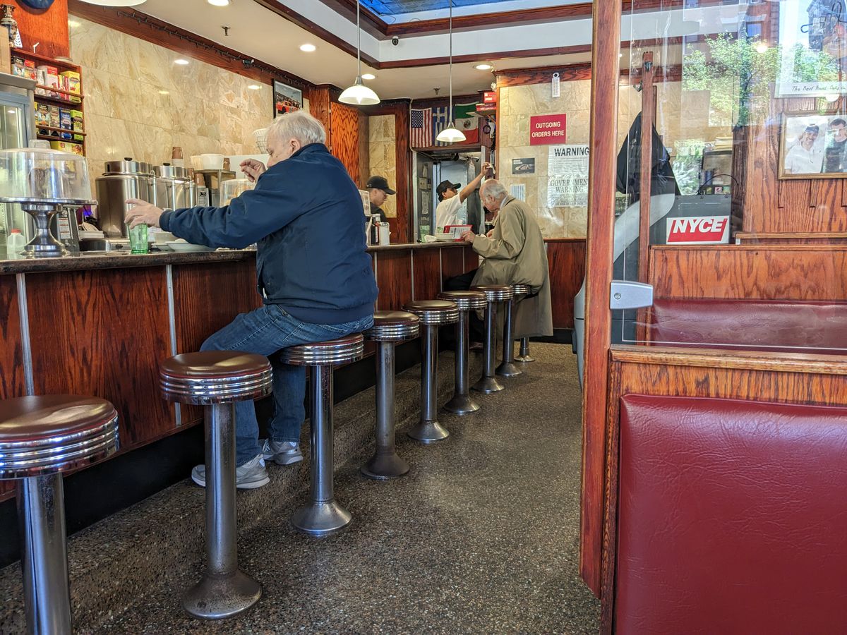 A lunch counter with twirling stools at which an old man sits.