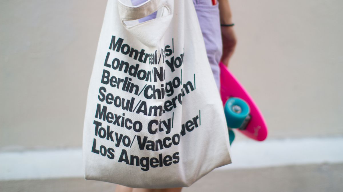 A person carrying a white American Apparel tote bag and skateboard.