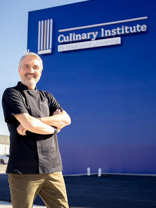 A chef posing in front of a blue building. 