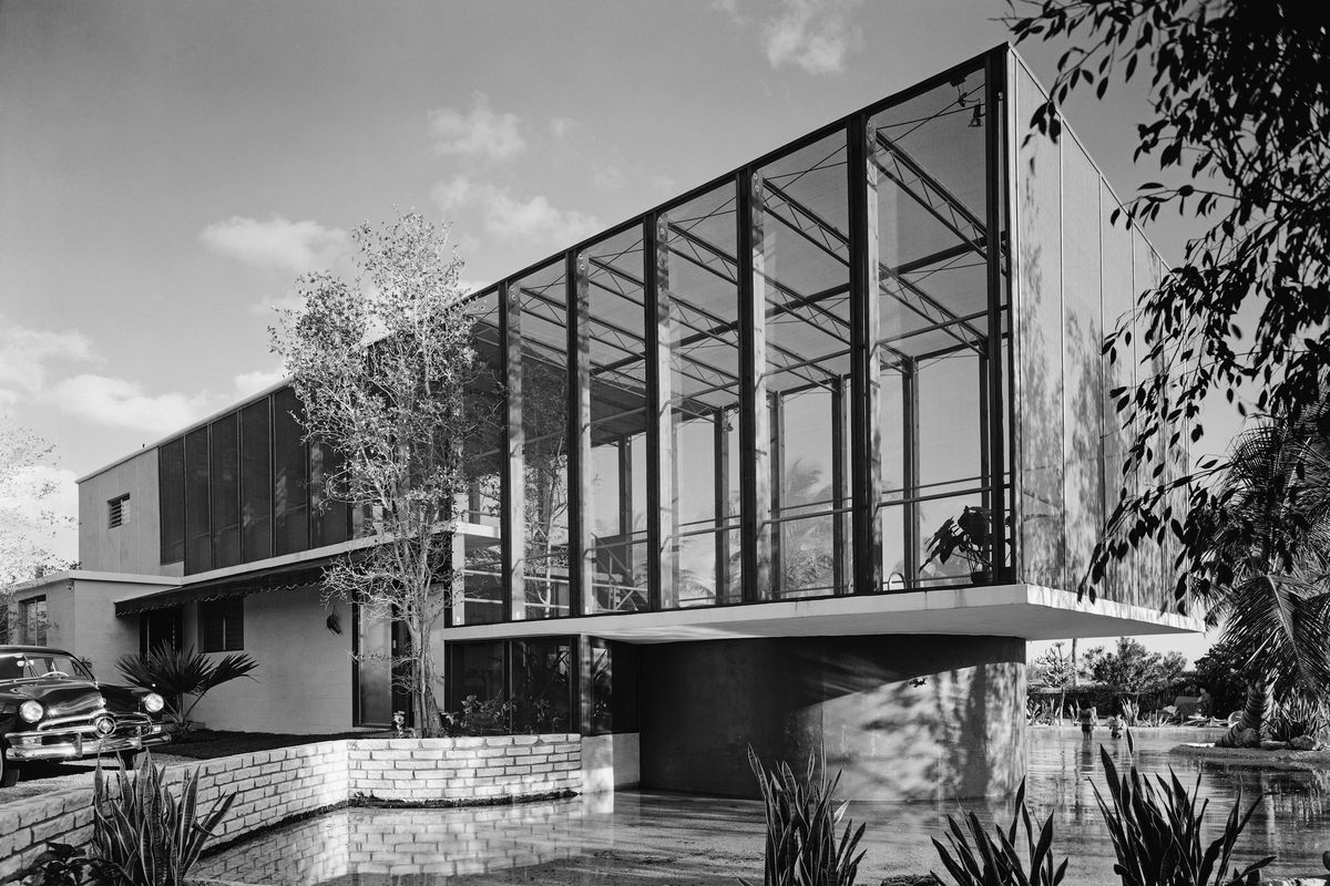 Black and white photograph showing a modern building with large glass wall. 