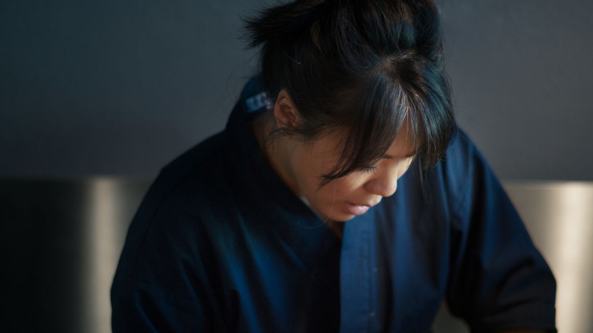 A Korean-American woman wearing a blue chef’s jacket, her hair in a ponytail, scoops rice at the counter of Zilla Sake