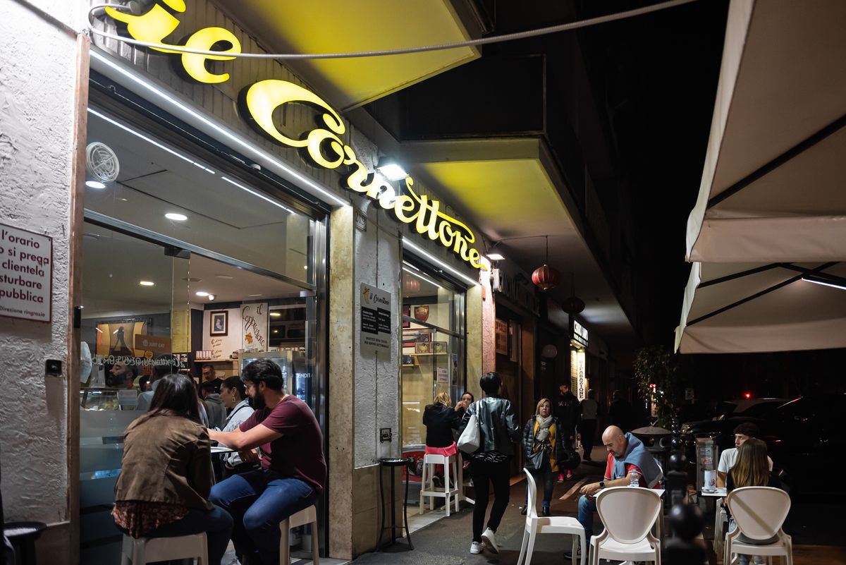 Customers sit at tables outside a bakery at night.
