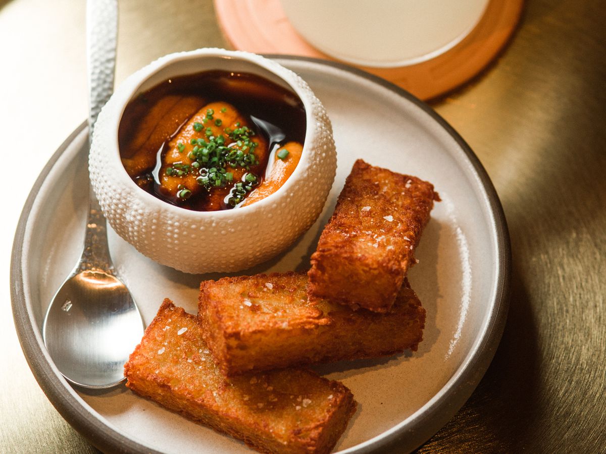 Rectangular fried wedges of potato croquettes, served on a plate with a small bowl of uni, alongside a white cocktail