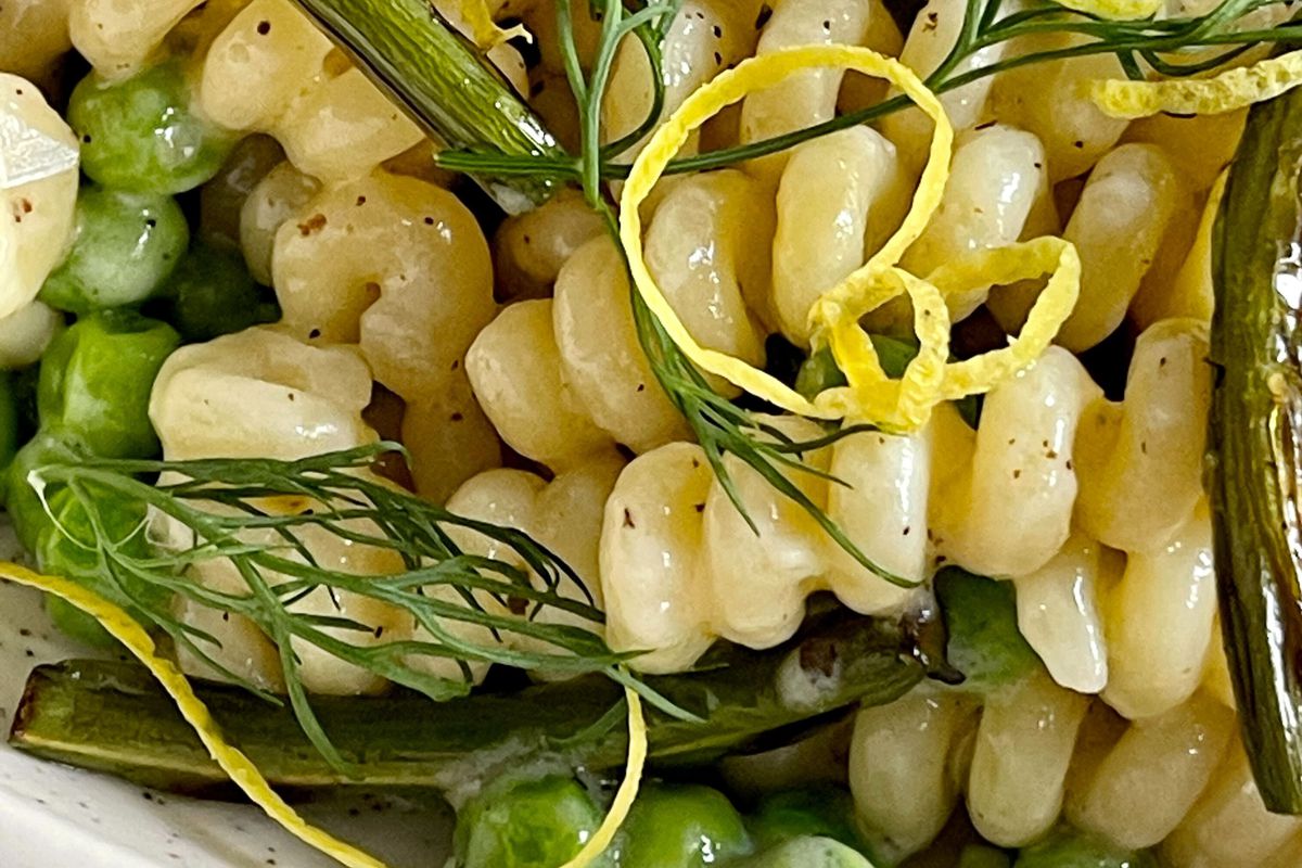 Close-up of a coil pasta shape cooked with peas and topped with dill and lemon peel.