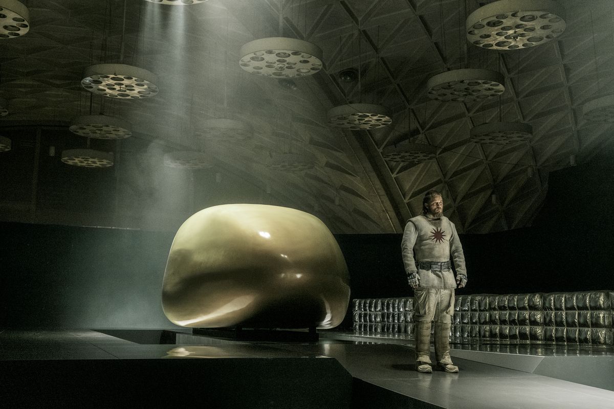 Travis Fimmel stands by a sleek, shiny space-pod in a weird space-hangar in Raised By Wolves.