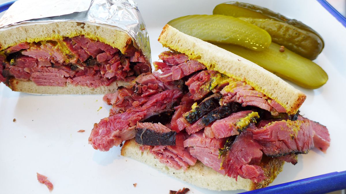 A jagged pastrami sandwich bursting with thick slices of deeply red pastrami, one half still wrapped in foil.