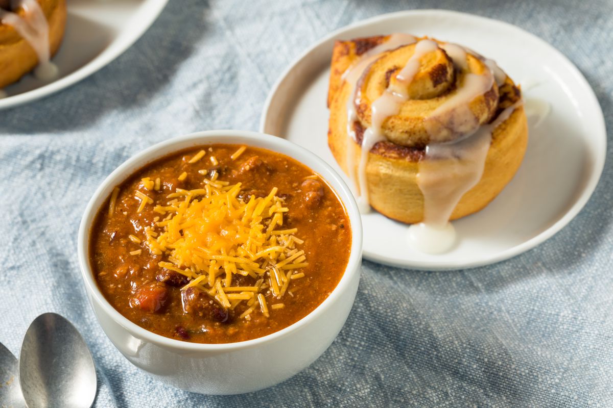 A bowl of cheese-topped chili and a cinnamon roll.