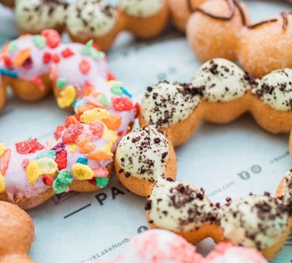 Close-up view of several mochinut doughnuts, covered with various including, including chocolatey cookie or brownie crumbs and colorful cereal puffs.