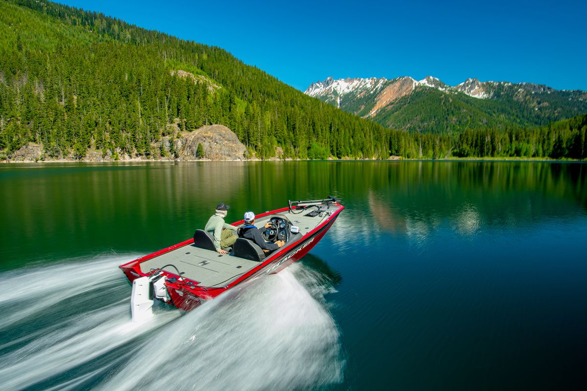 An electric speed boat zooming across a lake surrounded by forested hills.
