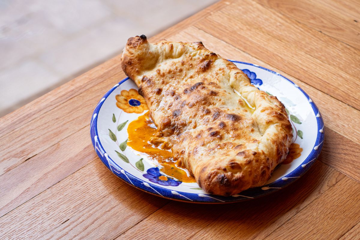 A baked and folded naan bread pocket on a blue and white plate stuffed with orange butter chicken sauce.