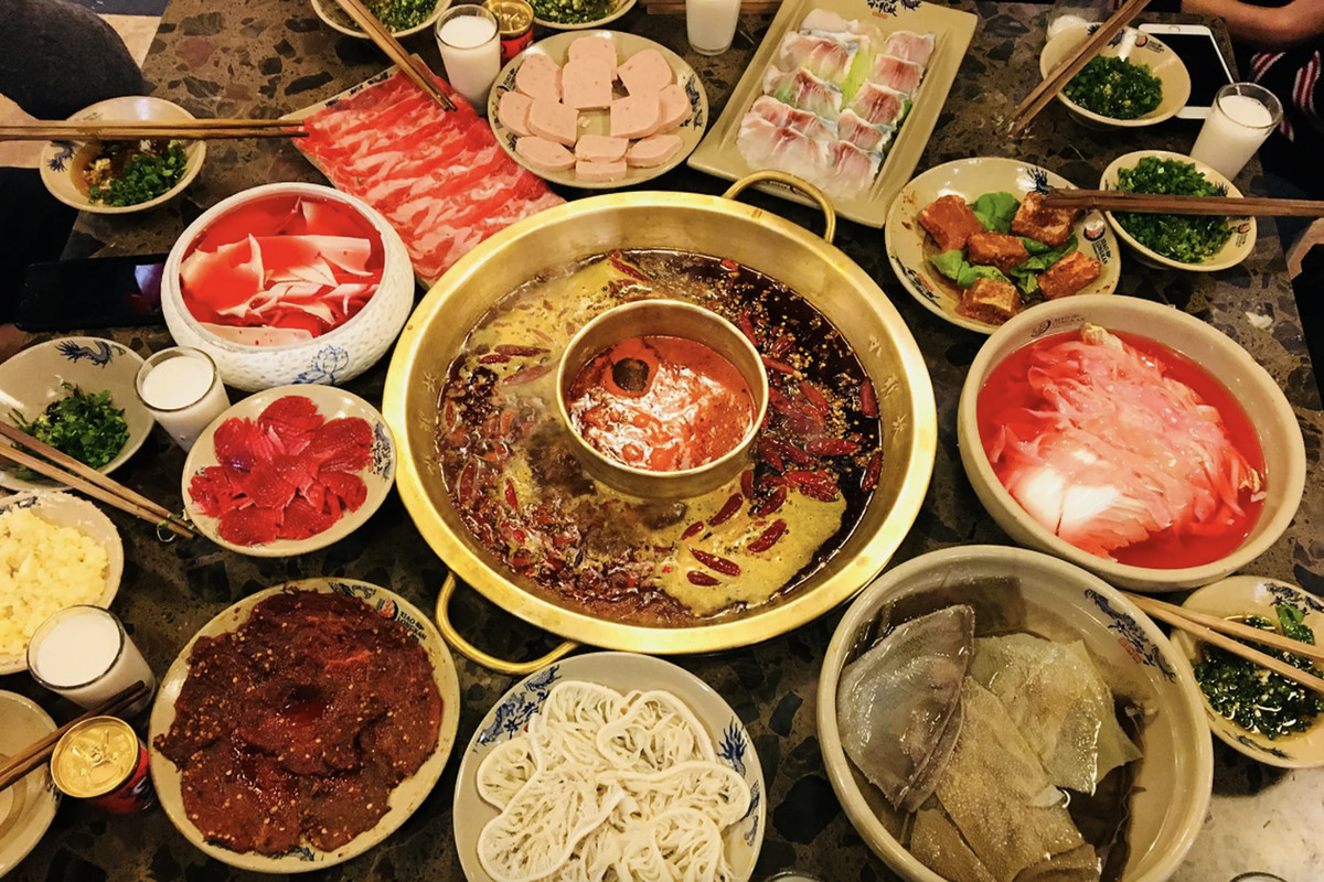 A crowded tabletop filled with a Chinese hotpot and plates of ingredients.