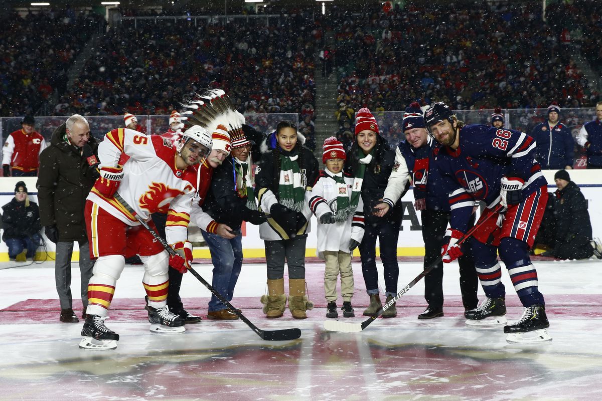Mark Giordano of the Calgary Flames, Lanny McDonald, Fred Sasakamoose, Brigette Lacquette, two local youth players and Blake Wheeler of the Winnipeg Jets take part in the ceremonial puck during the 2019 Tim Hortons NHL Heritage Classic at Mosaic Stadium on October 26, 2019 in Regina, Canada.