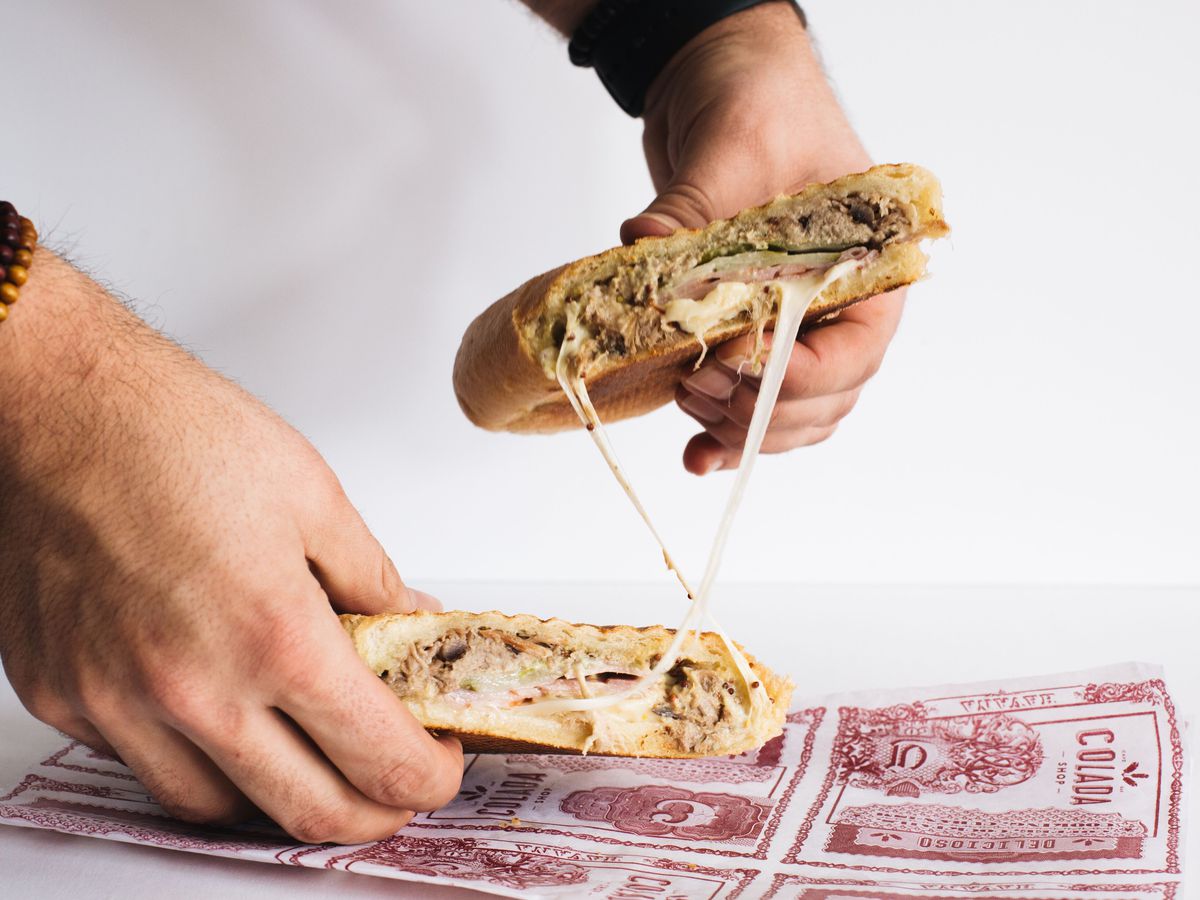 A Cuban sandwich, cut in half and being stretched apart