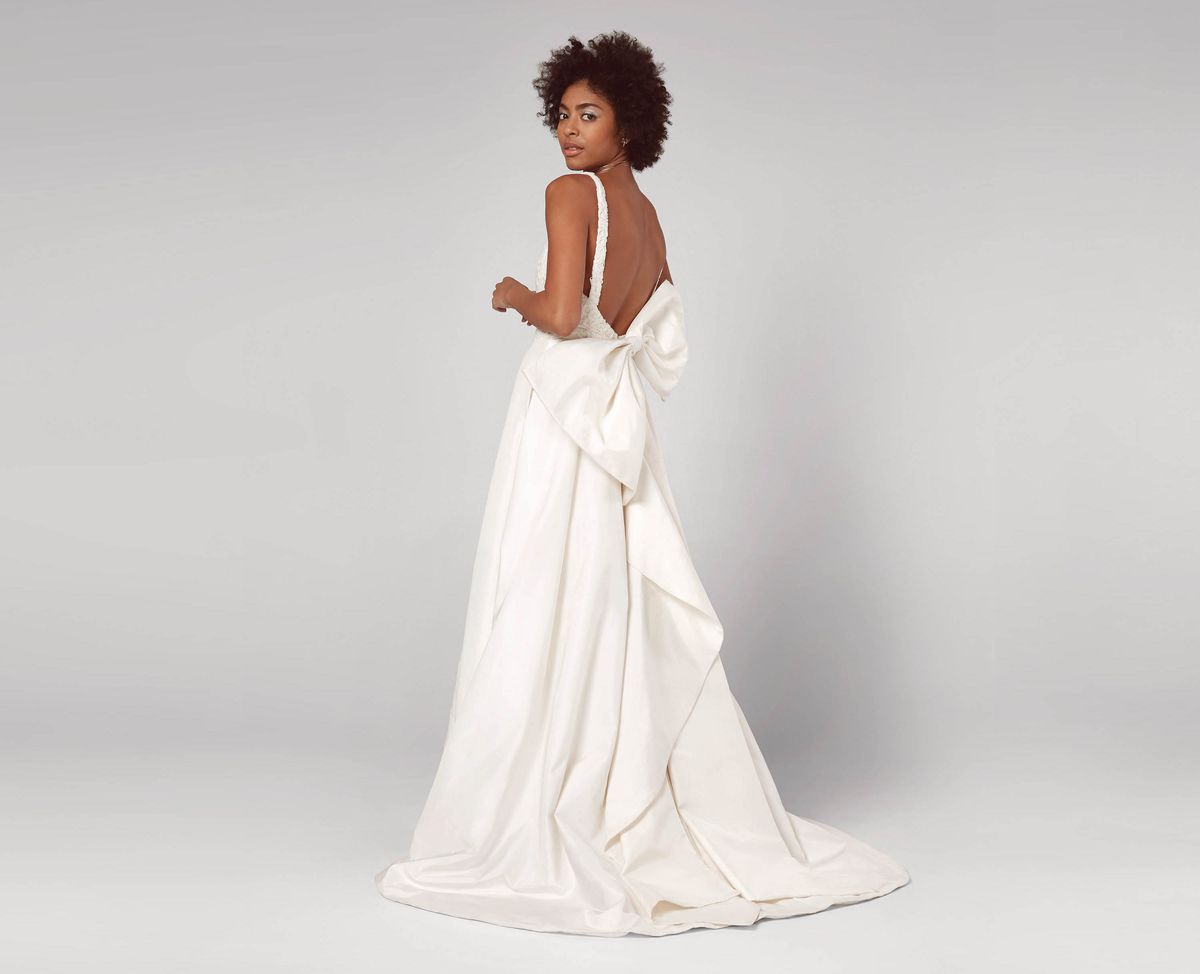 A model wearing a white wedding gown with an open back and big bow detail 