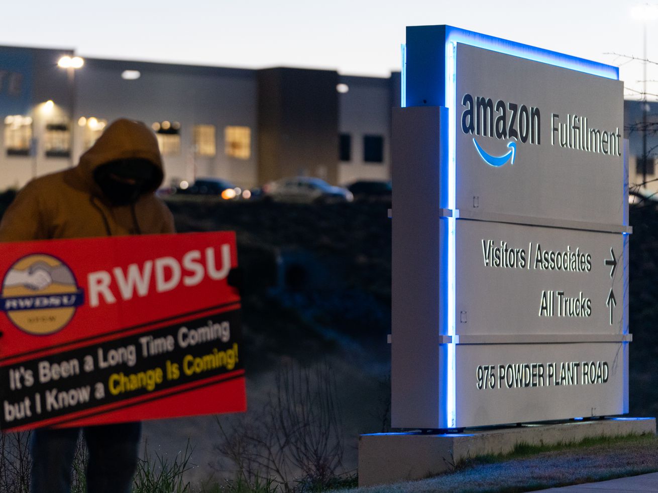An RWDSU union representative holds a sign that reads “RWDSU: It’s been a long time coming but I know a change is coming” outside the Amazon fulfillment warehouse at the center of a unionization drive on March 29, 2021, in Bessemer, Alabama.