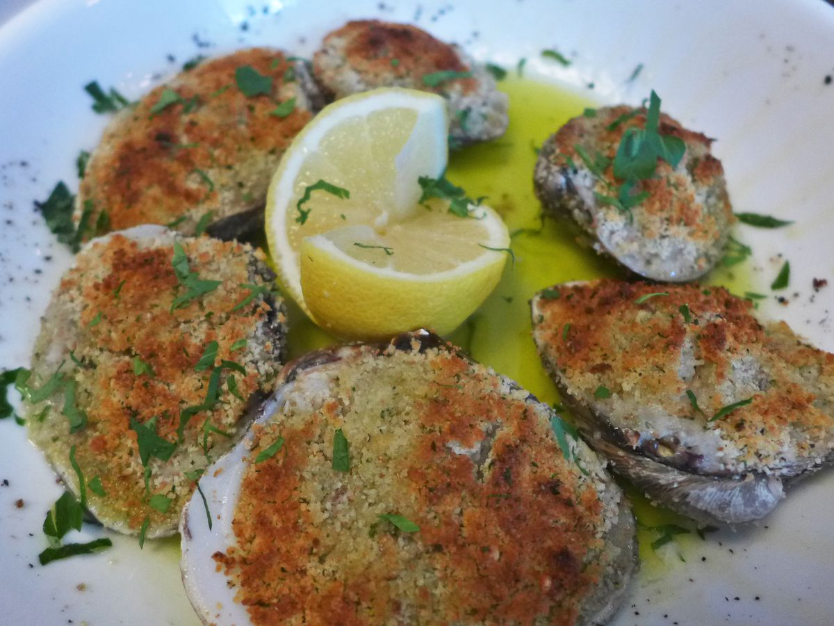 A half dozen baked clams with a bread crumb stuffing spilling out.