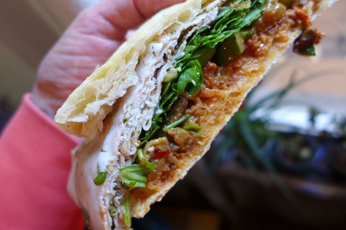A sandwich cut in half to reveal layers of slice meat, arugula, and pureed salami.