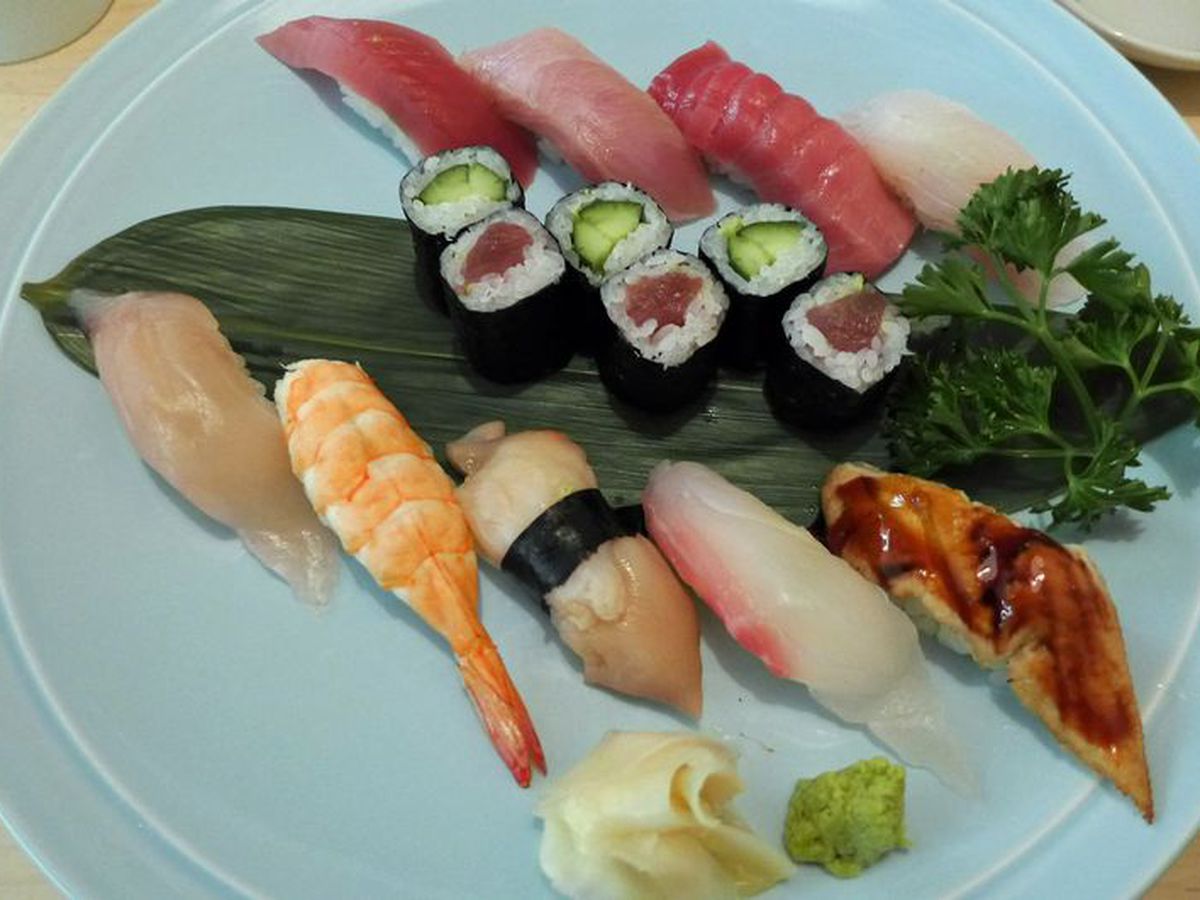 An assortment of raw fish and six pieces of sushi next to ginger and wasabi