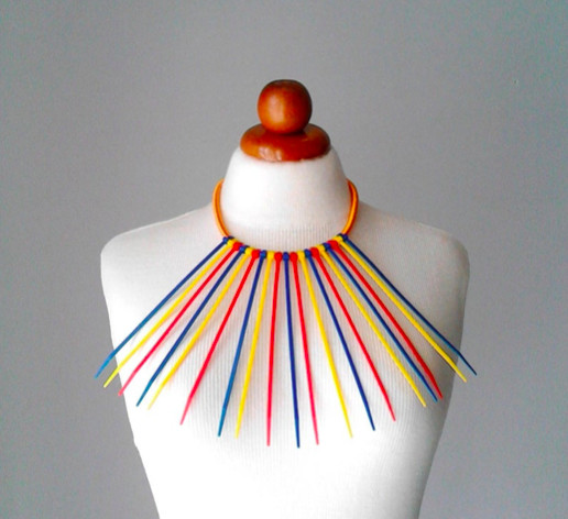 Necklace displayed on a bust with blue, yellow, and red zip ties hanging from a silk cord.
