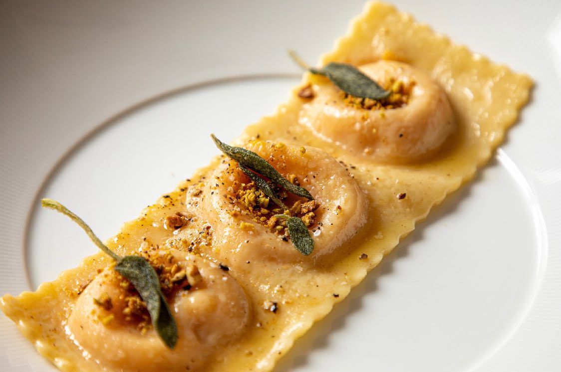 Three pieces of sweet potato ravioli with brown butter, pistachio, and sage on a white plate