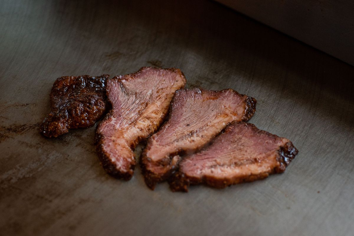 Three pieces of thick cut brisket on a griddle at a restaurant.