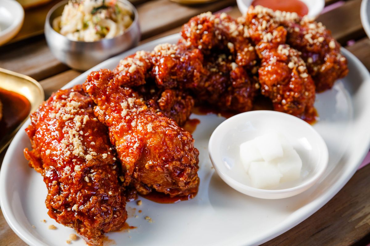 Sweet gochujang sauce coats large fried chicken piece sitting on a white plate with daikon radish cubes