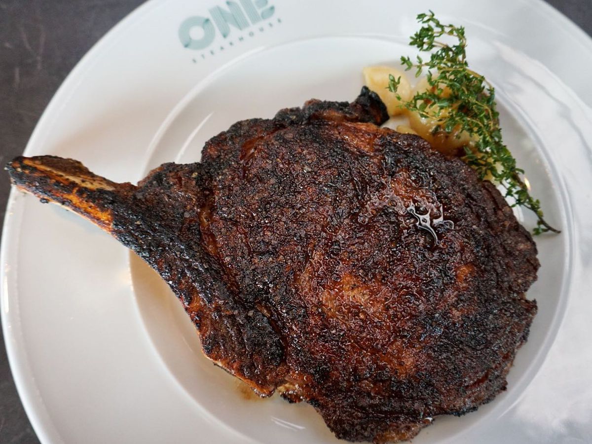 A 24-ounce bone-in rib-eye steak on a white plate.