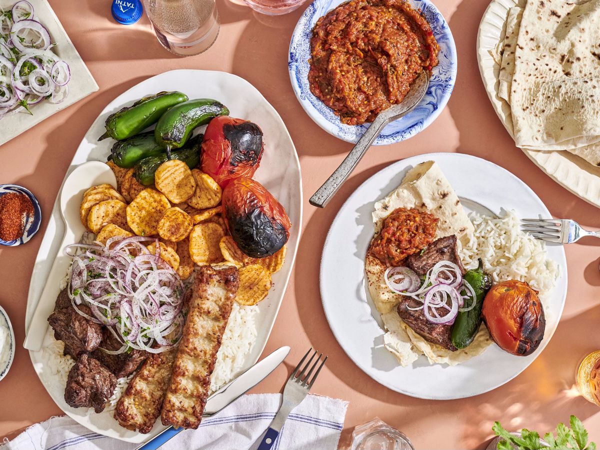 A photo of kebabs, vegetables, pitas on a platter