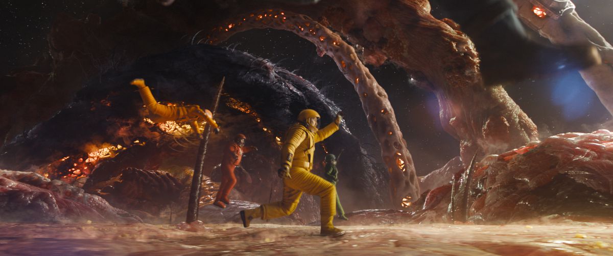 Mantis (Pom Klementieff), Drax (Dave Bautista), Peter Quill/Star-Lord (Chris Pratt), and Nebula (Karen Gillan) leap and stride across the low-gravity surface of a huge biological structure, covered in a fleshy surface with huge hairs and bones growing out of it in Guardians of the Galaxy Vol. 3.