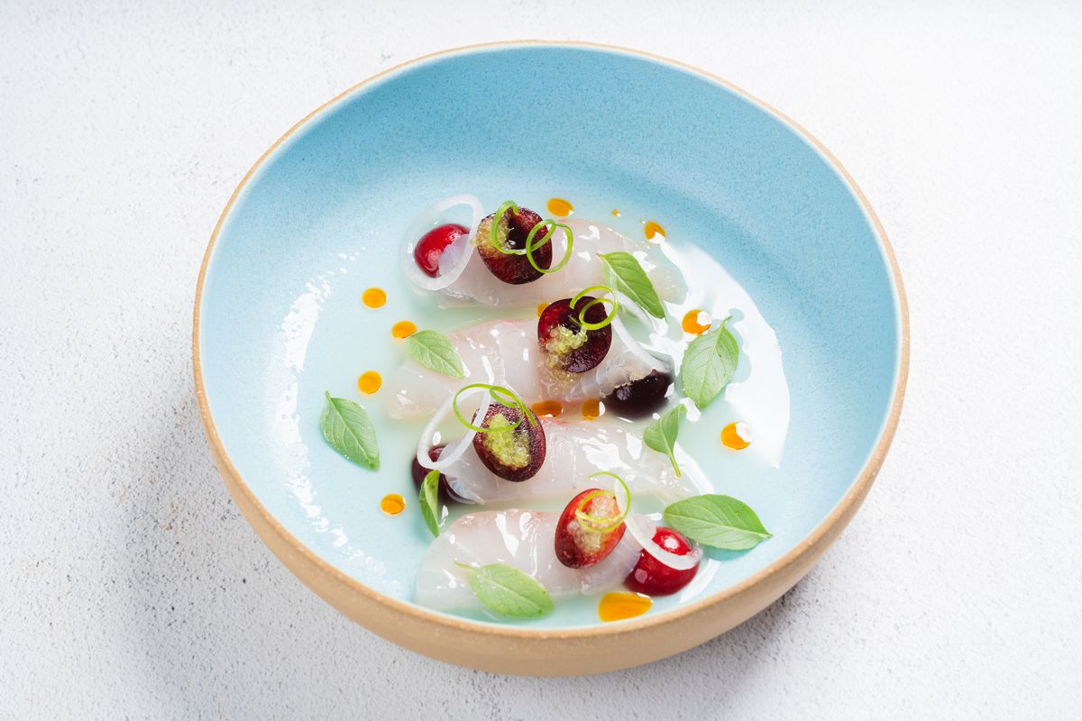 A bowl of halibut crudo garnished with cherries.