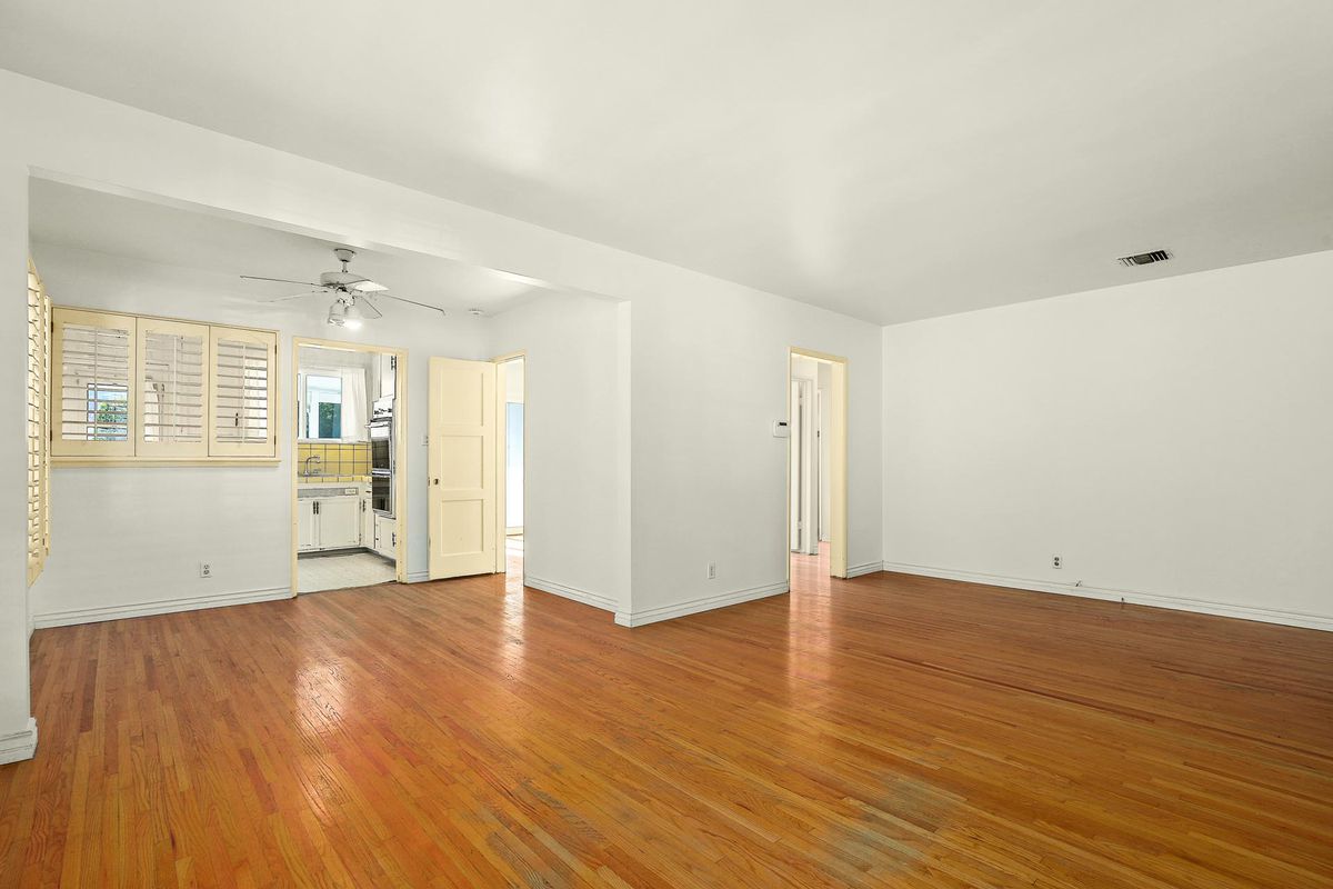 A large open room with hardwood floors. The kitchen is visible just beyond the end of the hardwood. 