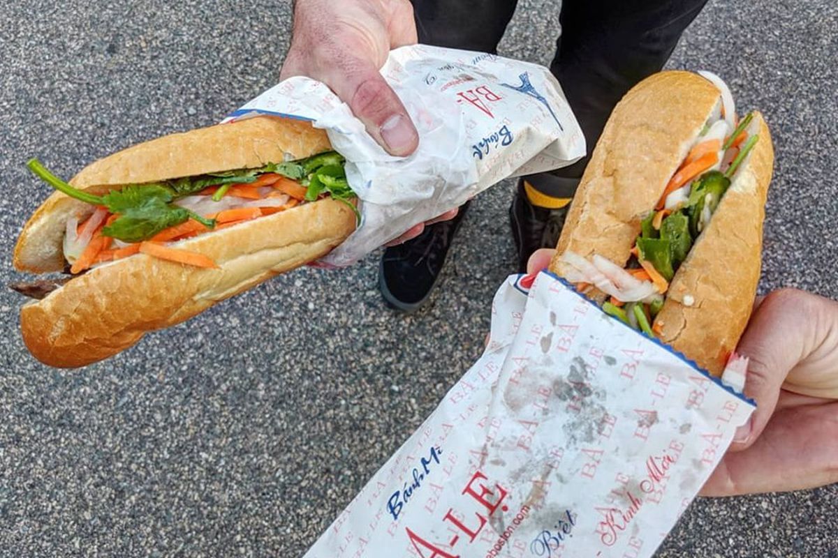 Hands hold two banh mi over pavement